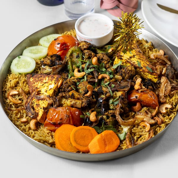 Pariwaar Delights' paneer biryani with grilled vegetables, cashews, and a side of raita.
