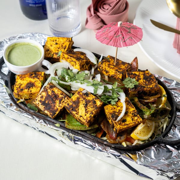 Sizzling paneer tikka with onions, cilantro, and a lemon wedge, served with green chutney.