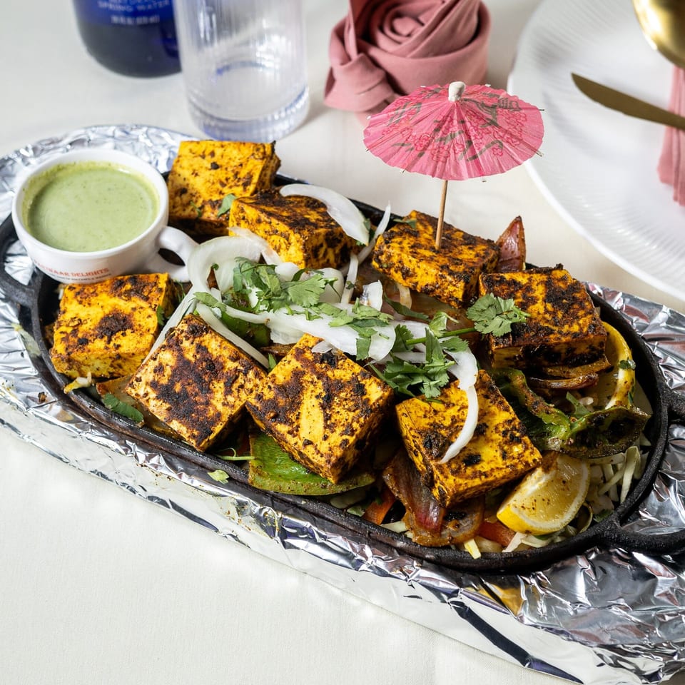 Sizzling paneer tikka with onions, cilantro, and a lemon wedge, served with green chutney.
